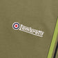 Close-up of olive green fabric with a white embroidered Lambretta logo and a red, white, and blue target emblem.