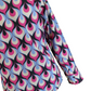 A long-sleeve button-up shirt featuring a bold 1970s-style peacock feather pattern in pink, light blue, cream, and black, shown against a plain white background.