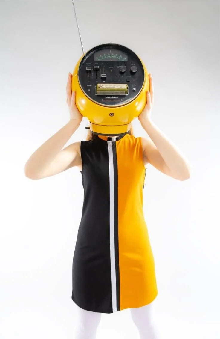Person wearing a black and yellow dress with a large round object on their head against a white background